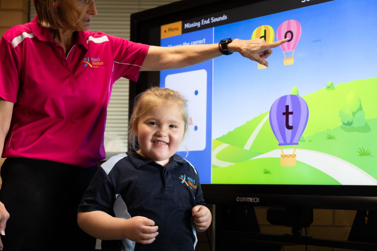 Student smiles at the camera infront of an interactive whiteboard